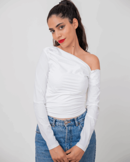 Model wearing a white asymmetrical top in a standing pose, showcasing the front design.
